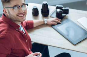 Happy freelancer man sitting by working table with graphic tablet