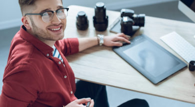Happy freelancer man sitting by working table with graphic tablet