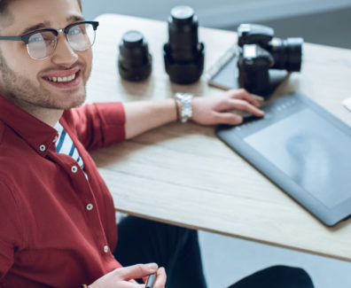 Happy freelancer man sitting by working table with graphic tablet