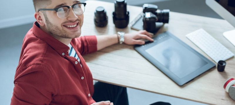 Happy freelancer man sitting by working table with graphic tablet